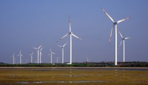 Under a cloudless sky there are numerous wind turbines with three immense blades per turbine in use along a vast marsh.