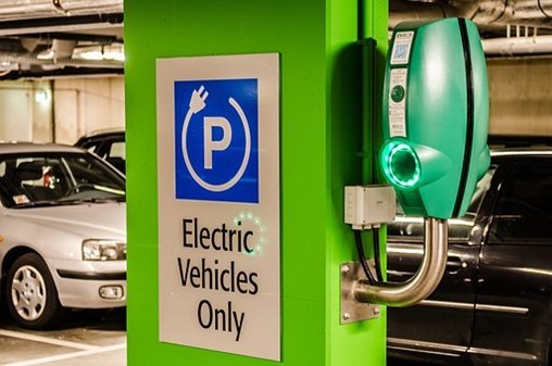 A bright green column in a parking garage has a sign that reads “electric vehicles only,” and the column has a green charger lit up with neon lights where the charger inserts.