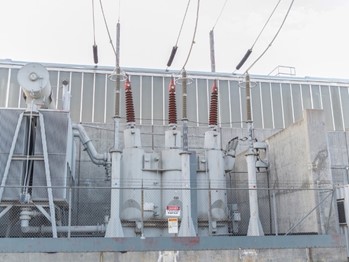 Electrical lines attach to a transformer station with a surrounding fence and a danger sign.