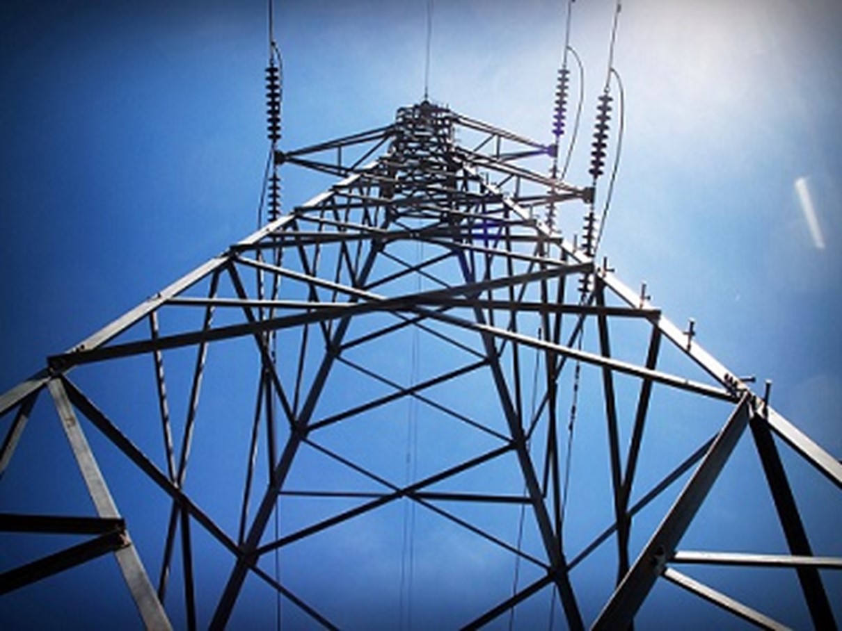 A close-up photograph of a power line tower from the ground looking skyward.