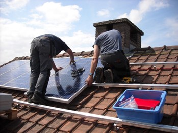 Two people on a Spanish-style tiled roof installing solar panels on a sunny day.