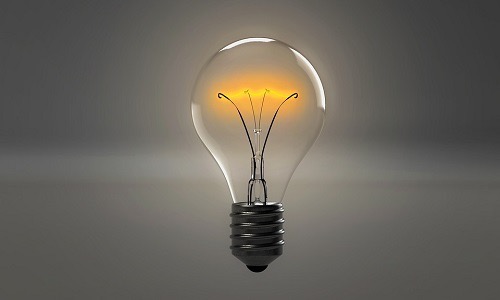 A floating standard light bulb glowing with a warm yellow light against a gray backdrop.