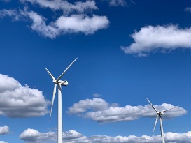 Two wind turbines photographed in front of a blue sky with a few white clouds.