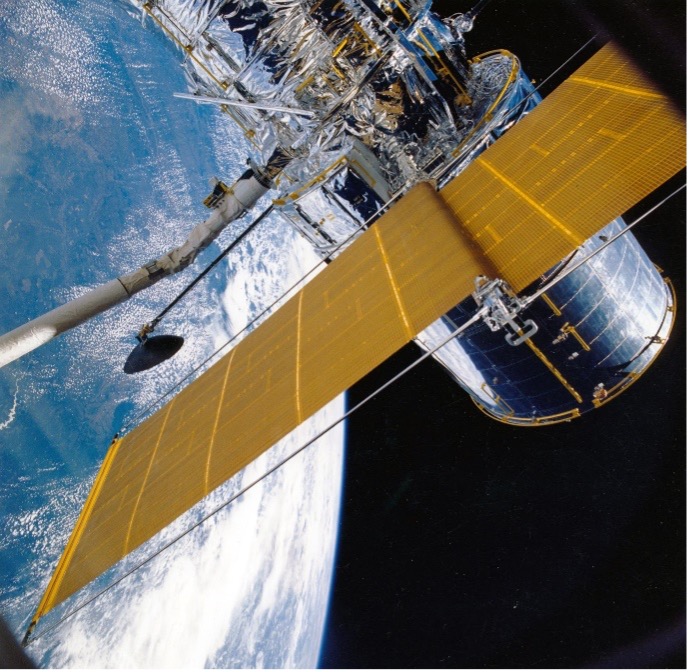 A slanted gold satellite floating in space with Earth and starry outerspace behind it.