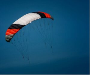 Photo of a cloudless dark blue sky and a massive grey, red, black, and white power kite. The kite appears to be blowing towards the left side of the photo.
