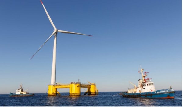 A wind turbine on floaters, also known as WindFloat, is being monitored by two ships at a wind farm in the ocean.