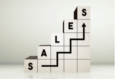The image shows a creative arrangement of three-dimensional blocks forming a staircase-like graph, with the letters S, A, L, E, and S written on the side of the blocks. An upward arrow traces a path over the blocks, representing an increase in sales or success in sales growth.